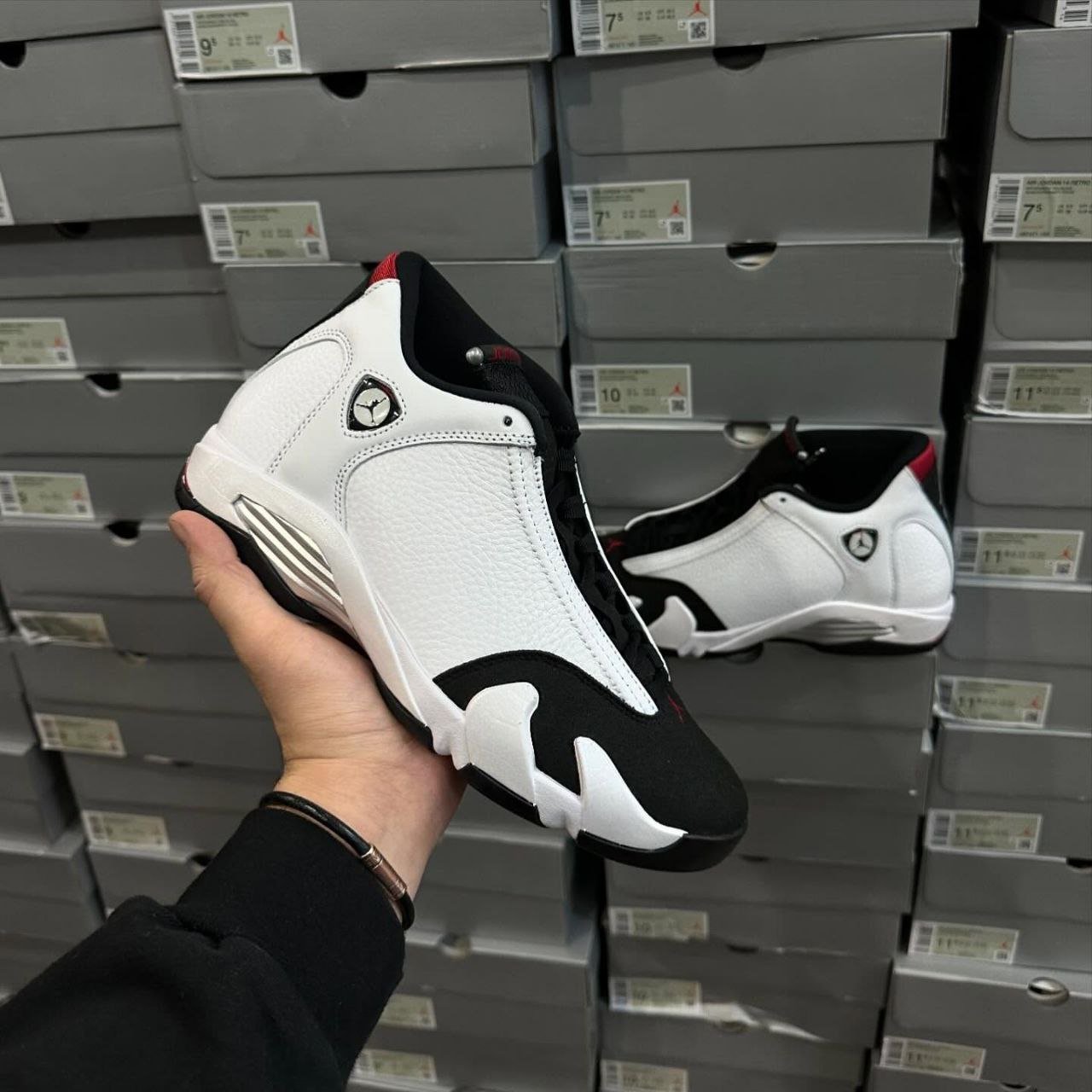 Air Jordan Retro Pallets for sale - Pallet Liquidation Okc Person holding a white and black athletic sneaker with a Jumpman logo, in front of stacked shoeboxes in a store.